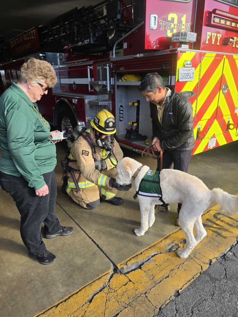 A HOPE Animal-Assisted Crisis Response dog interacts with a firefighter outside a fire truck, as the handler and another team member observe, demonstrating evaluation of the dog's comfort around emergency equipment.