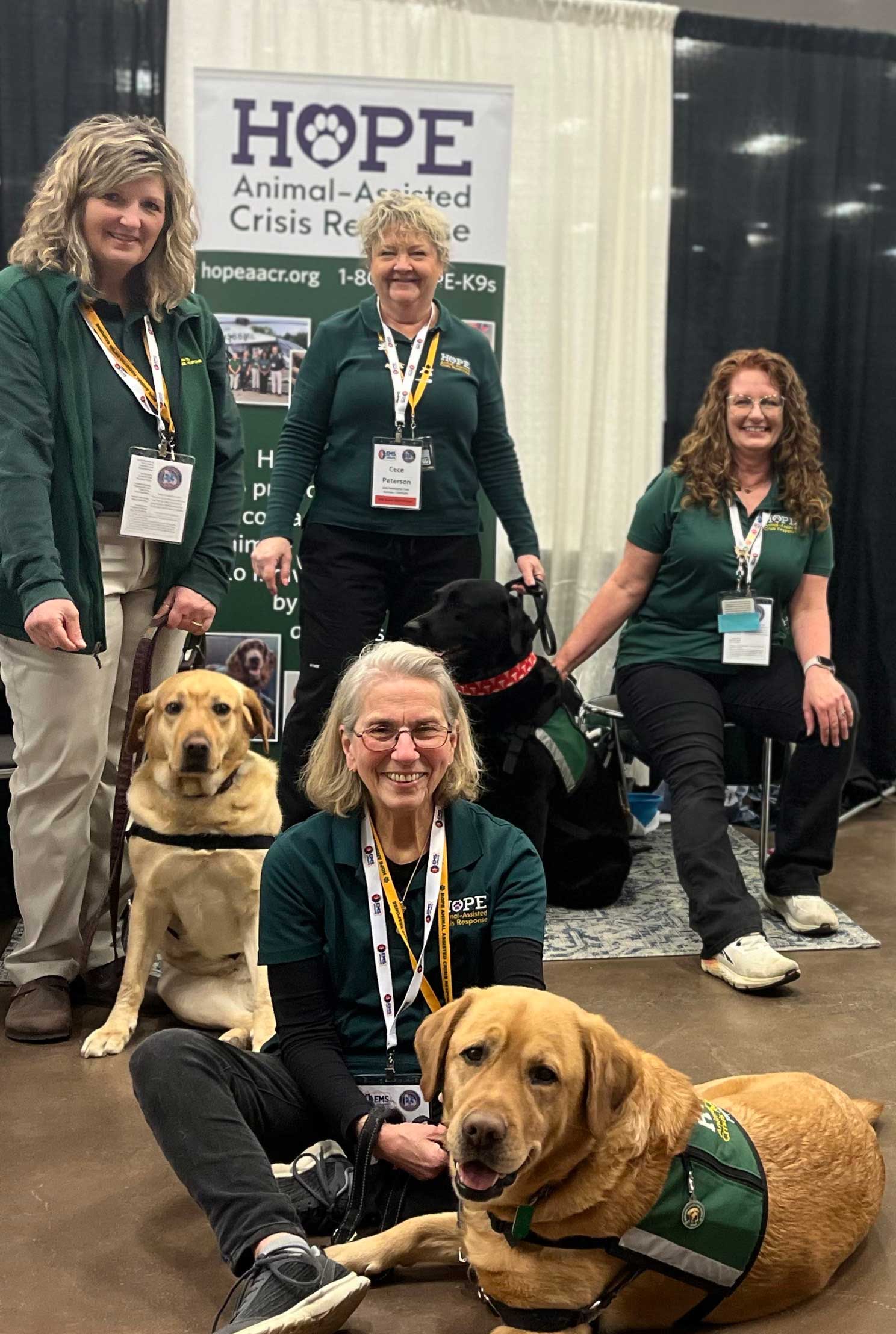 HOPE Animal-Assisted Crisis Response volunteers pose with their dogs in front of an informational booth, representing the organization at a public event.